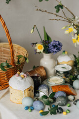 Stylish Easter eggs, bread and basket with spring flowers on rustic table. Happy Easter! Traditional easter holiday food for blessing. Modern natural dye eggs, tasty ham, bread, butter, beets