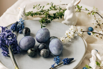 Stylish easter eggs on vintage plate, bunny and spring flowers on rustic table. Happy Easter! Natural dye blue eggs, purple hiacynt blossoms on linen napkin. Holiday setting, minimal still life