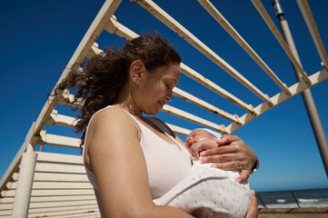 Woman carrying her newborn baby while walking together on the city on warm sunny day