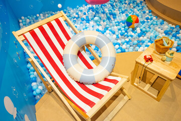 Striped deck chair and swimming rubber ring near children ball pool,Red beach sunbed in Summertime...