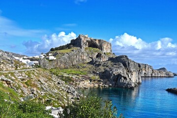 view of the blue sea, the remains of the fortress and the rocks above the sea from a distance where you can also see part of the settlement by the sea on a nice sunny day