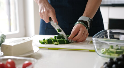 Woman'S Hands Are Slicing Cucumber For Greek Salad With A Glass Of White Wine Nearby - 755112094
