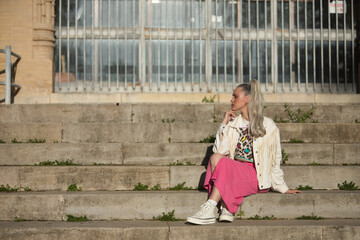 Young, pretty, blonde woman, with blue eyes, white fringed jacket and pink skirt, with her hand on...