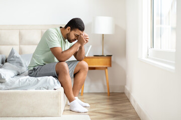 Unhappy african american guy suffering from loneliness, bedroom interior