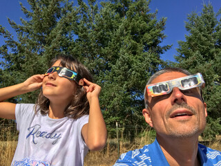 A young girl with her father looking at the sun during a solar eclipse on a country park, family outdoor activity - 755115235