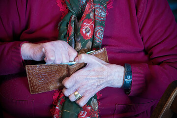 An elderly woman searching for money in her wallet at home - 755116487