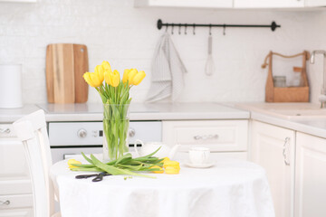 Home kitchen interior.Vase with bouquet of yellow tulips, teapot, sissors on table. Spring consept.