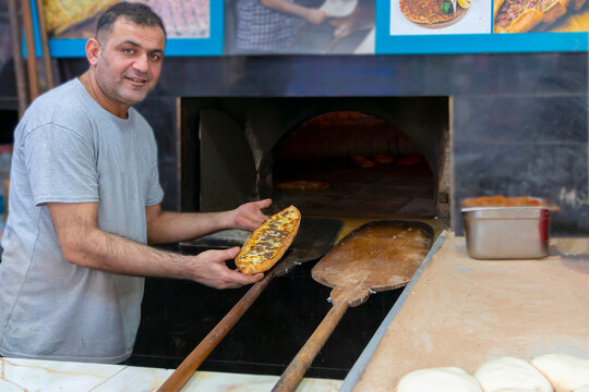 A mature baker taking pizza with special shovel from oven. Traditional turkish pizza, pida is roasted in a wood-fired oven. Concept - preparing and roasting  pizza