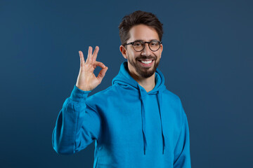 Naklejka premium Happy Young Man Wearing Blue Hoodie Showing Ok Gesture At Camera