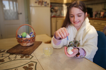 Happy cute little girl decorating Easter eggs using brush and paint on the kitchen. 