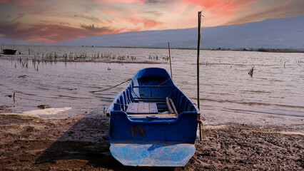 Clouds with sunlight on sunset time over the lake landscape and the old blue fishing boats with...