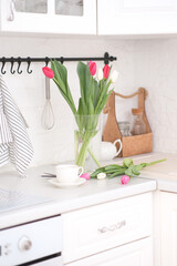 Home kitchen interior.Vase with bouquet of pink and white tulips, glass of tea, teapot on white worktop of kitchen cupboard. Spring consept.