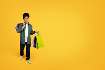 Excited african american guy with purchases walking on yellow