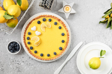 Traditional French lemon pie with blueberries on a white stone background.