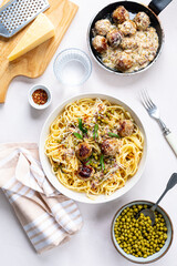 Spaghetti with meatballs and cream sauce is served on a plate with herbs and parmesan.