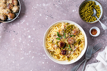 Spaghetti with meatballs and cream sauce is served on a plate with herbs and parmesan.