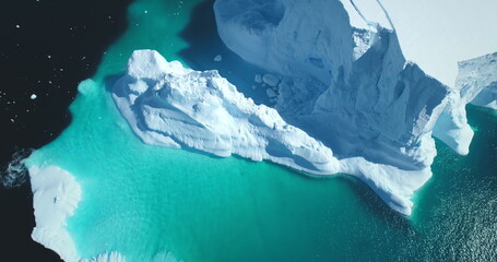 Melting snow covered glacier in blue water aerial top view. Nature beauty towering floating iceberg. Polar winter landscape. Ecology, melting ice, climate change, global warming background. Drone shot