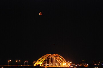 Lit up bridge with lunar eclipse happening above it