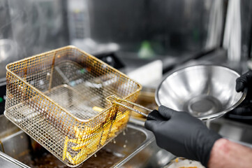 Freshly fried golden French fries being transferred from a metal basket to a stainless steel bowl...