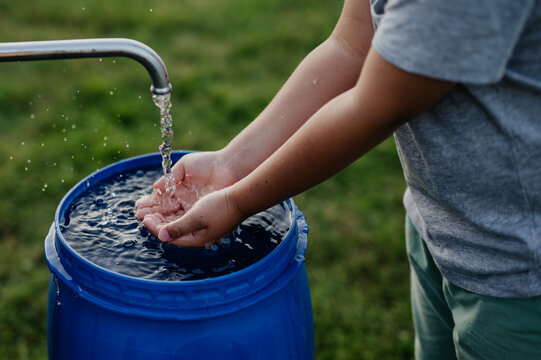 Boy washing his hands with water from a well. Well with a pump for outdoor washing in garden.