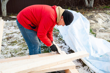 A man in a red jacket is engaged in construction using wooden planks - 755147497
