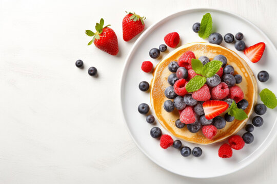 Plate with stack of pancakes with fresh strawberries, blueberries and raspberries and mint leaves, white marble table, top view