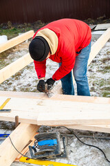 A man in a red jacket is engaged in construction using wooden planks