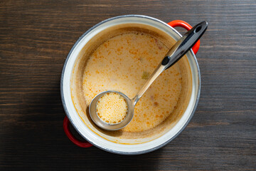 Leftovers cream fish soup in a saucepan with a ladle on a wooden table, closeup, top view