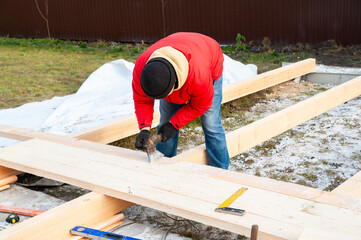 A man in a red jacket is engaged in construction using wooden planks - 755148493