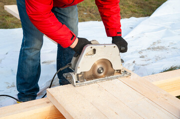A man in a red jacket cuts boards with a circular saw - 755150059