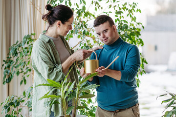 Portrait of young man with Down syndrome with mother, watering houseplant, taking care of plants....