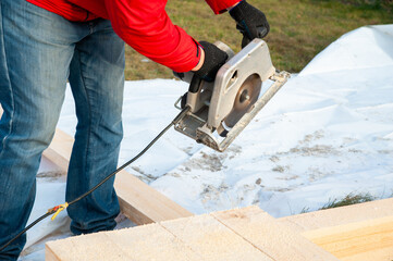 A man in a red jacket cuts boards with a circular saw - 755151232