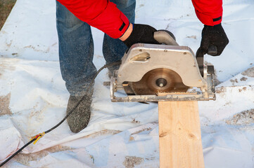 A man in a red jacket cuts boards with a circular saw - 755152803