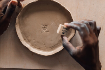 Interracial craftswoman's hands decorating handmade pottery at workshop