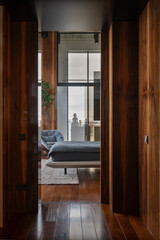 A hallway in a house with a bedroom featuring a bed and chair