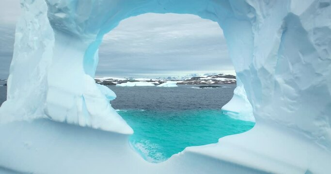 Huge hole in melting iceberg in Antarctic ocean close up. Flight inside frozen glacier cave arch window drifting blue cold water. Arctic winter landscape, global warming problem. Polar climate change