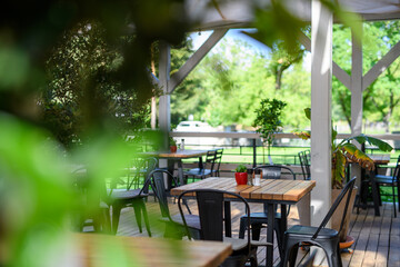 Covered summer terrace of a restaurant with wooden tables, chairs, and flooring. - 755173008