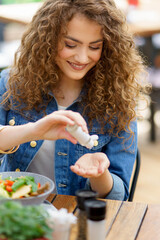 Beautiful woman sanitizing her hands with disinfectant gel in a restaurant before eating. Having lunch outdoors in restaurant patio. - 755173475