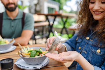 Beautiful woman sanitizing her hands with disinfectant gel in a restaurant before eating. Having lunch outdoors in restaurant patio. - 755173802