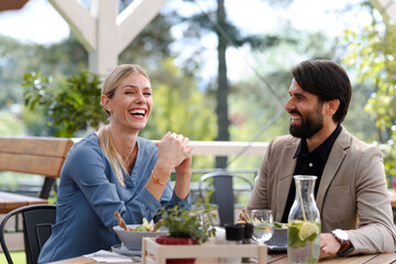 Couple sitting outdoors on terrace restaurant, having dinner date, laughing. Business lunch for two managers, discussing new business project. - 755174634