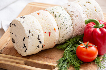 Closeup of several varieties of homemade cheese with different fillings with paprika, dill, olives, walnuts and cookies on a wooden board with fresh dill, tomatoes and bell pepper. - 755176072
