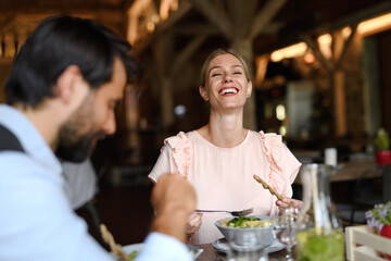 Happy loving couple at date in restaurant. Husband and wife sitting at table, laughing, having lunch in modern cafe. - 755176295