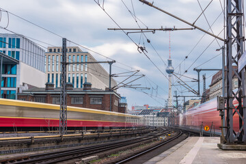 Trains in blur are leaving and approaching the station of Berlin Friedrichstrasse on a cool spring day. Typical houses and TV tower visible in the backgroubd. Train transport in germany, punctuality