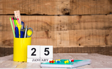 January calendar background with number  25. Stationery pens and pencils in a case on a wooden vintage background. Copy space notepad with pencils and a calendar. Planner place for text.