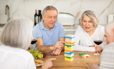 Group of happy seniors excitedly playing Jenga game at home