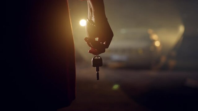 Close-up of car keys in the hand of an unrecognizable woman in a dark garage. A girl holds a retro car key in her hands at night indoors.