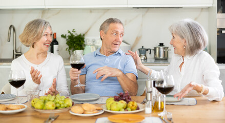 Happy pensioners gathered at the festive table - talking, discussing news and drinking red wine