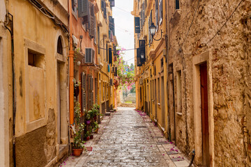 Kerkyra city narrow street view with yellow colorful houses and pink flowers during sunny day. Corfu Island, Ionian Sea, Greece.