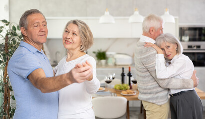 Obraz premium Elderly woman is dancing slow unhurried dance in hugs arms of her senior male partner. Senior men and women doing couple dancing during house party