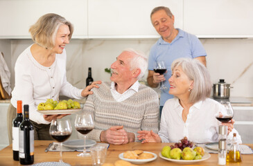 Fototapeta na wymiar Couples of elderly women and men chatting and drinking wine at table..